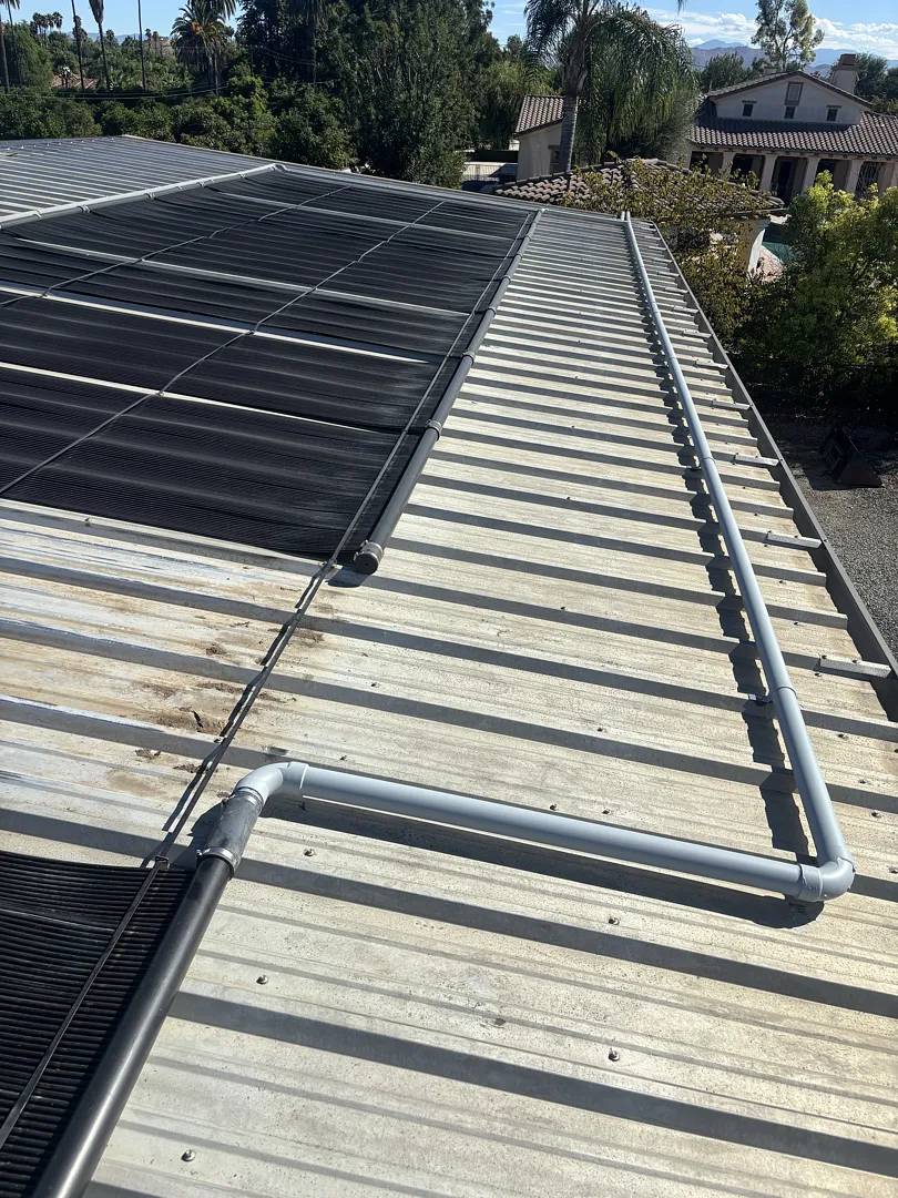 New gray PVC plumbing joining rows of solar pool heating panels on a corrugated metal roof in Riverside