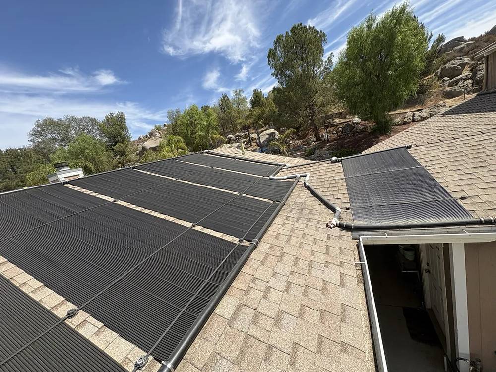 Solar pool heating panels on two faces of a shingle roof in Menifee, with boulder-covered hills behind