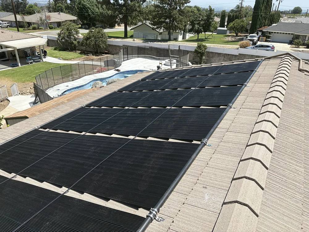 Solar pool heating panels on a tile roof in Rancho Cucamonga, above a backyard pool with a mesh safety fence